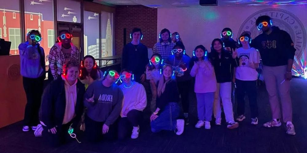 Students of the Campus Activities Board posing with glowing glasses and other accessories in a dark room